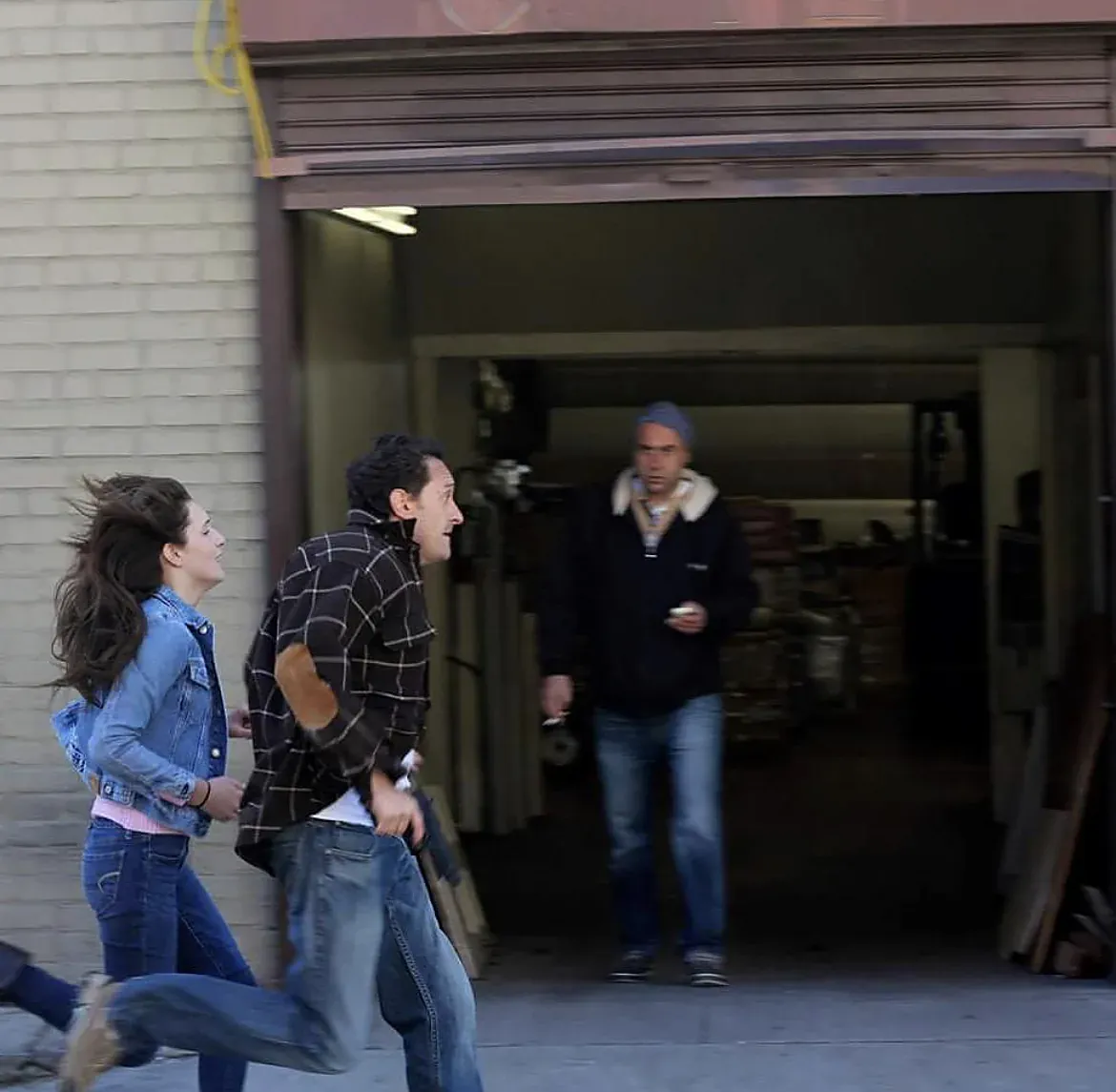 Two actors run past an open warehouse door in a chase scene